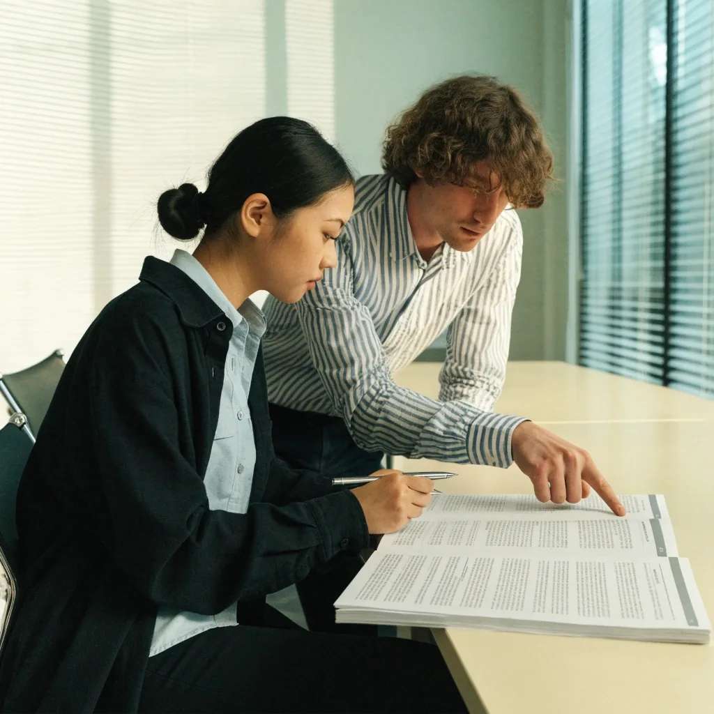 Two colleagues reviewing a printed policy handbook together in a meeting room